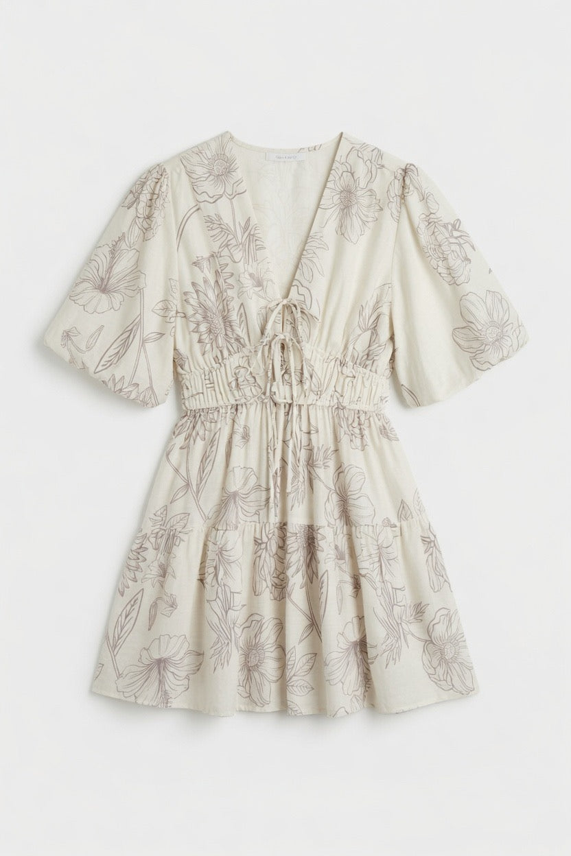 A short-sleeve cream-colored dress with a brown floral line-art print, featuring a V-neckline with a tie-front detail and a gathered smocked waist.
