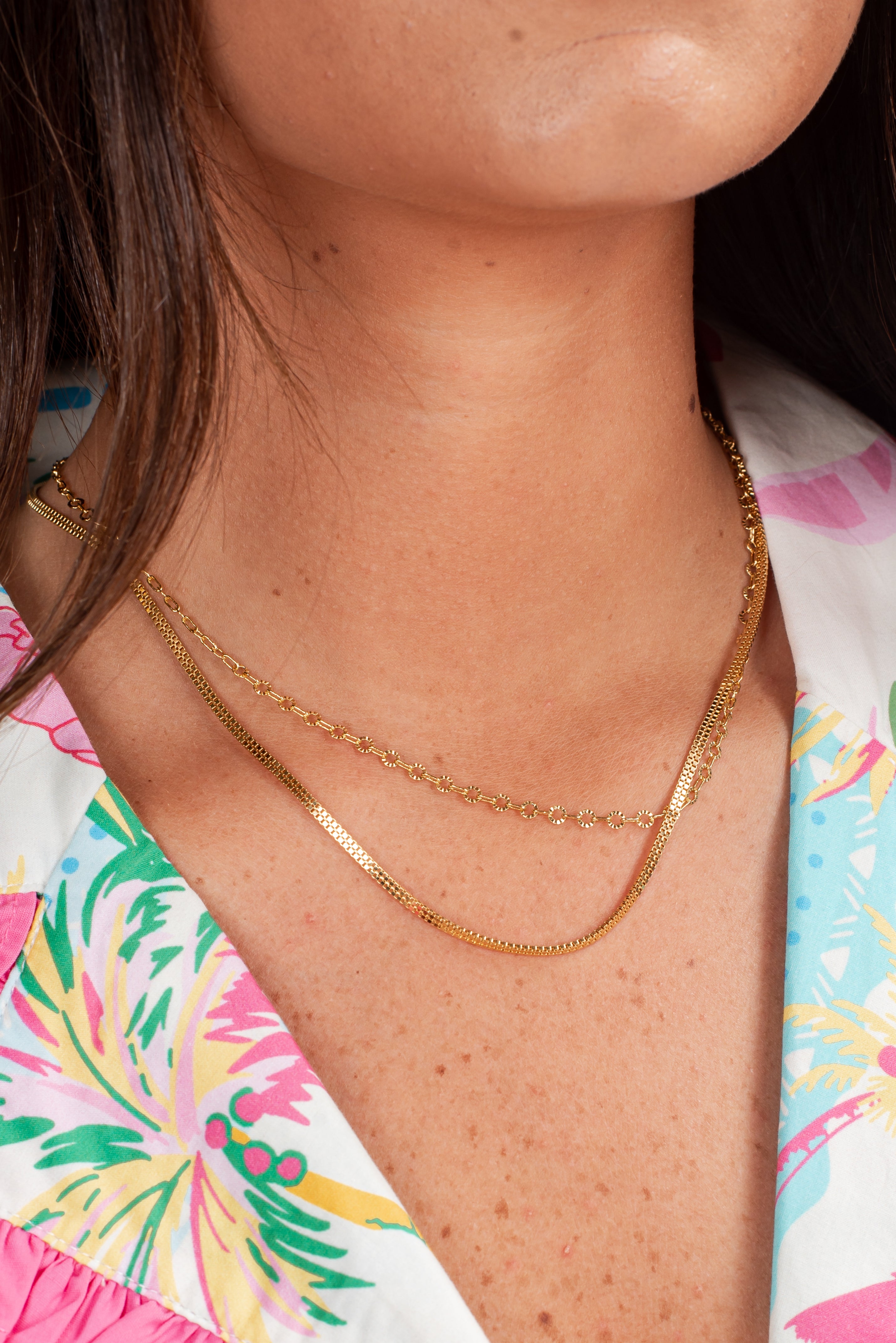 Close-up of a person wearing a gold necklace with a colorful garment in the background
