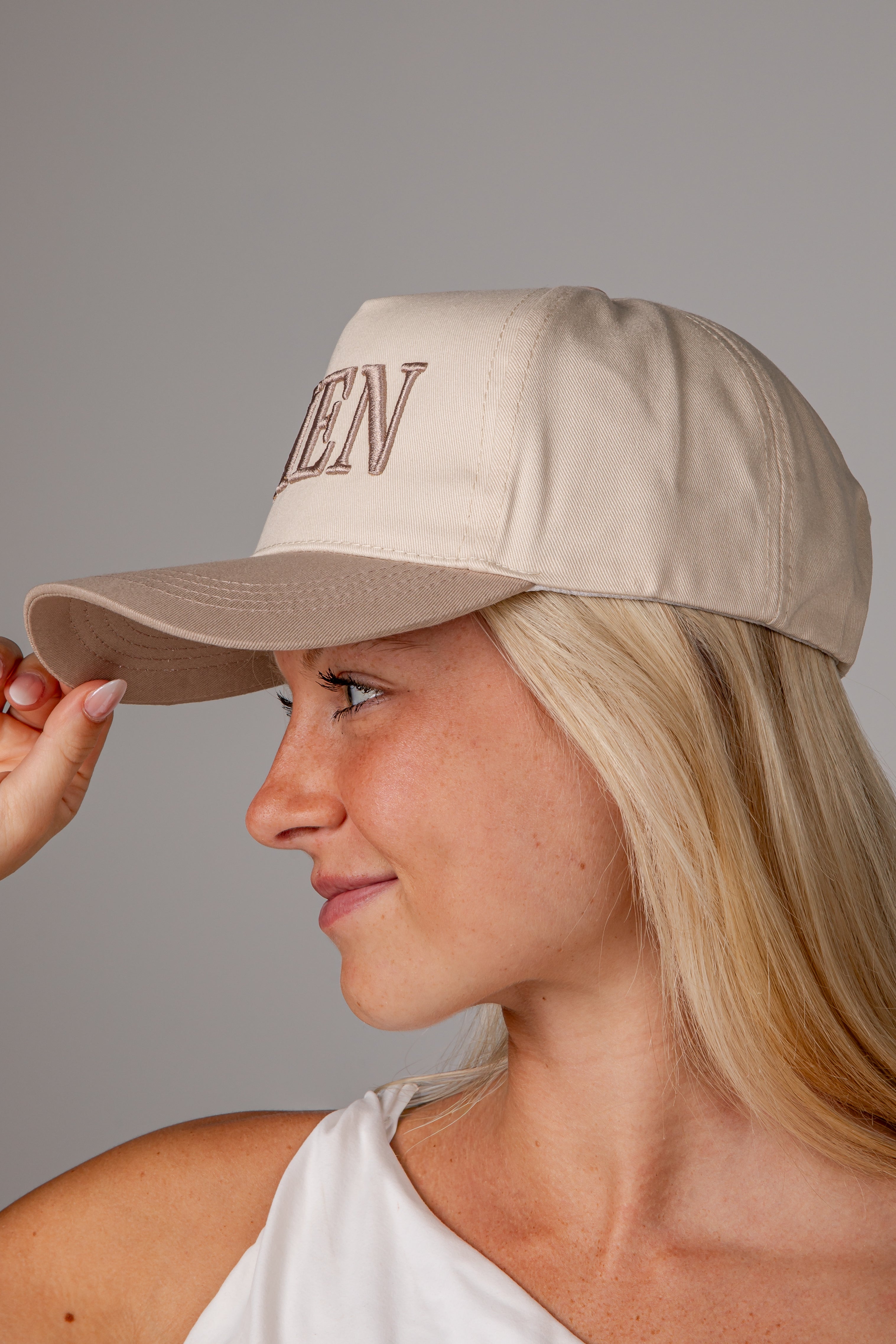 A woman in profile wearing a beige baseball cap with &