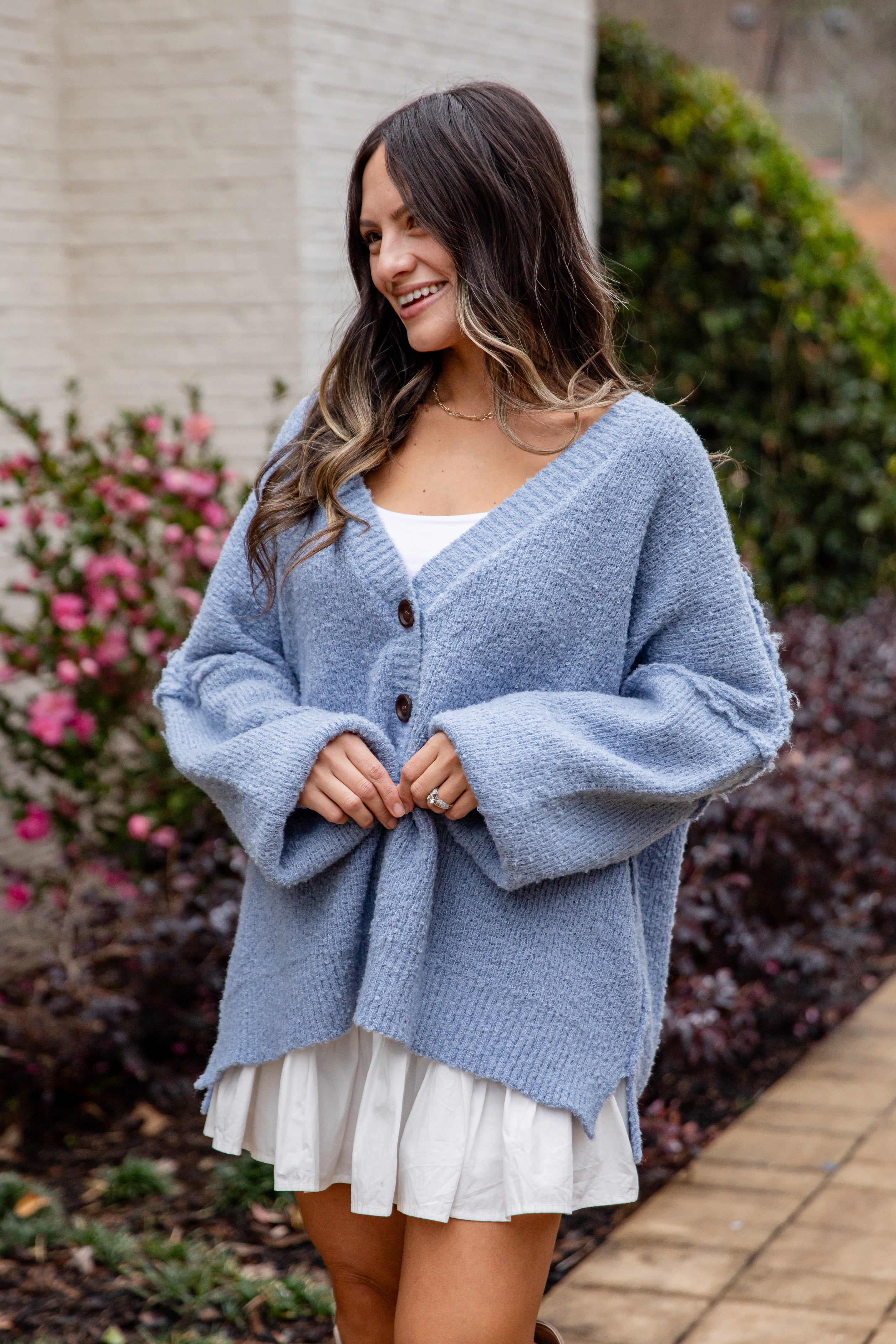 Woman wearing a blue cardigan over a white dress outdoors.