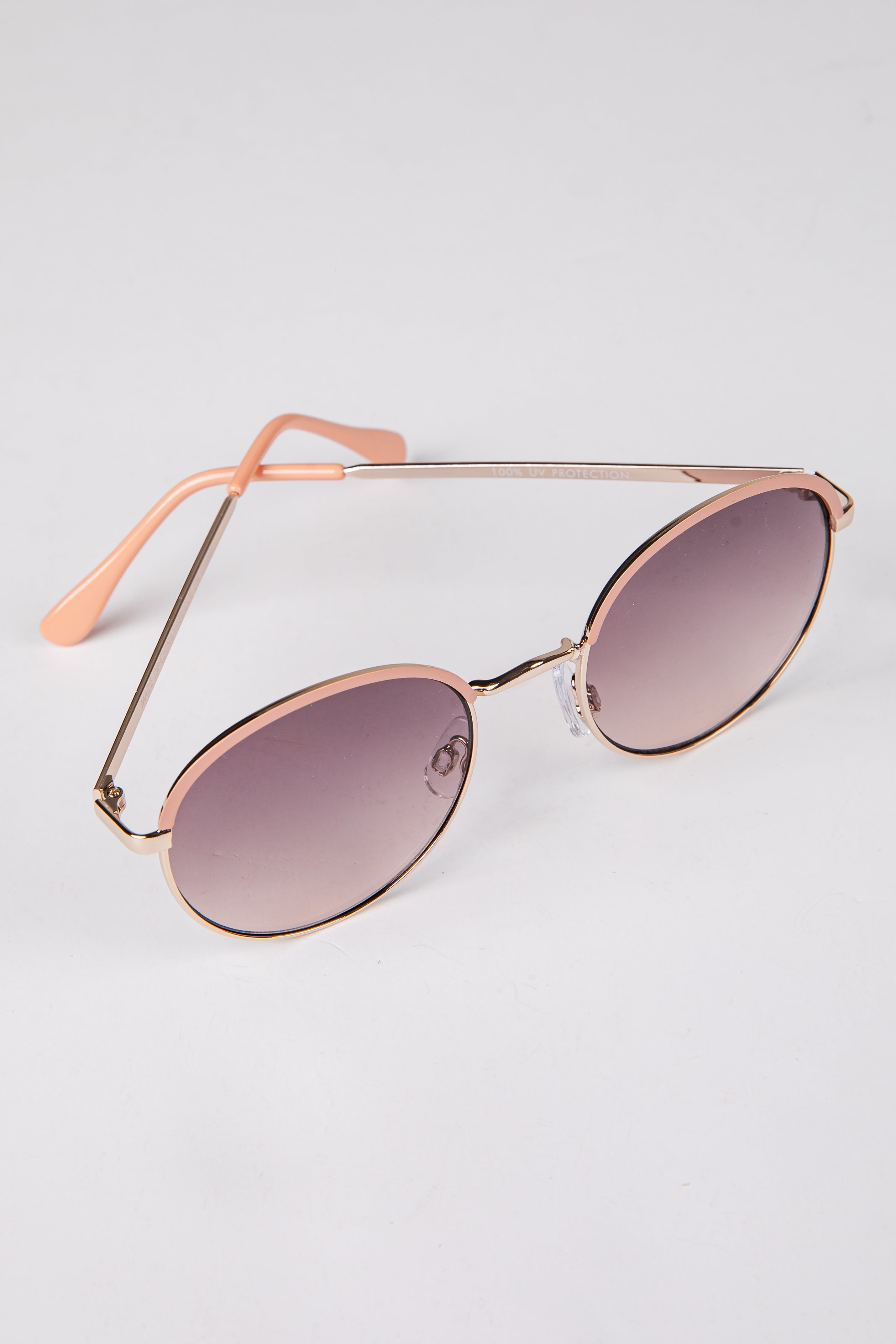 Sunglasses with rose gold frame and gradient lenses on a light gray background