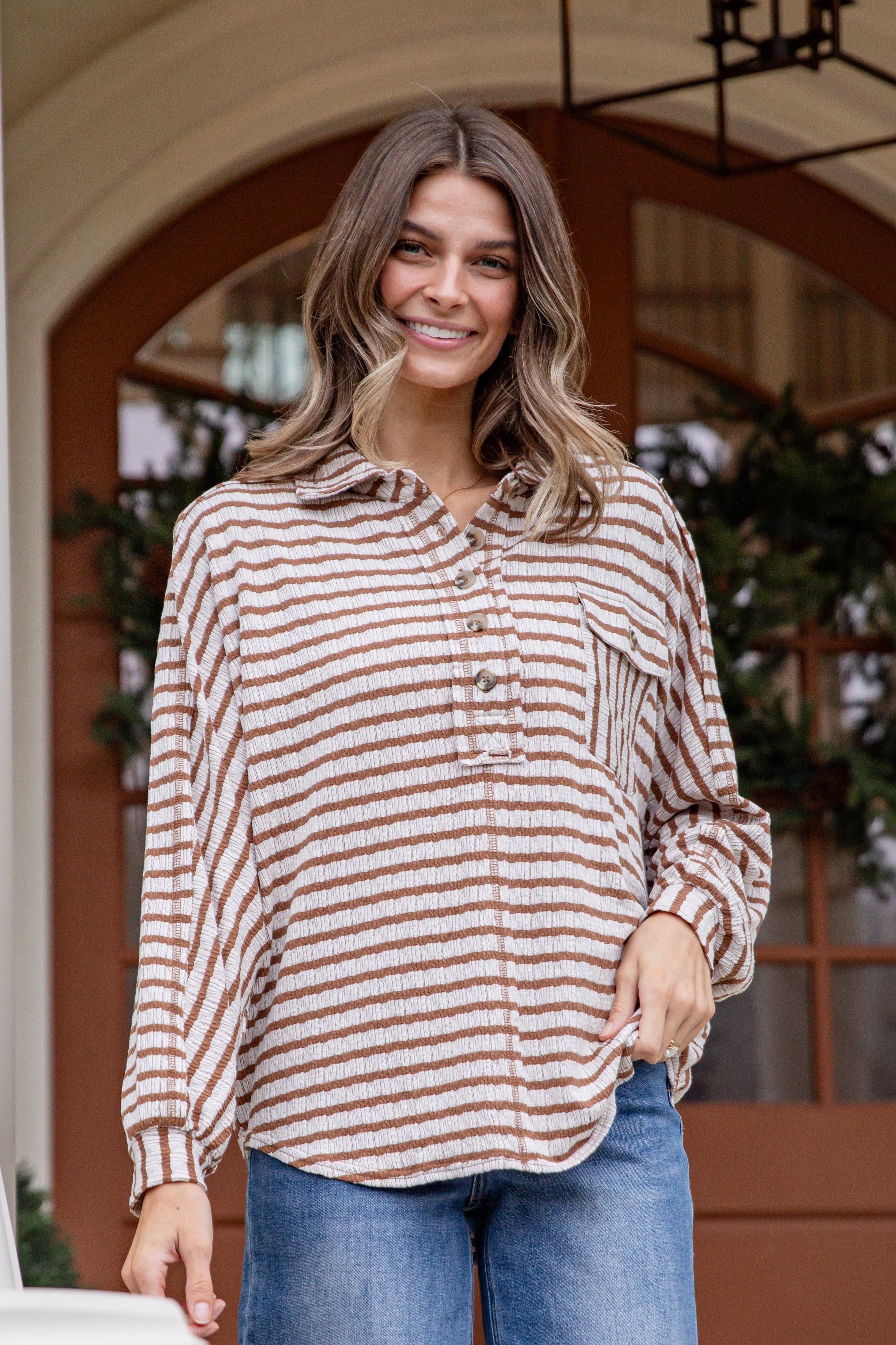 Woman wearing a striped shirt and jeans standing on a porch.