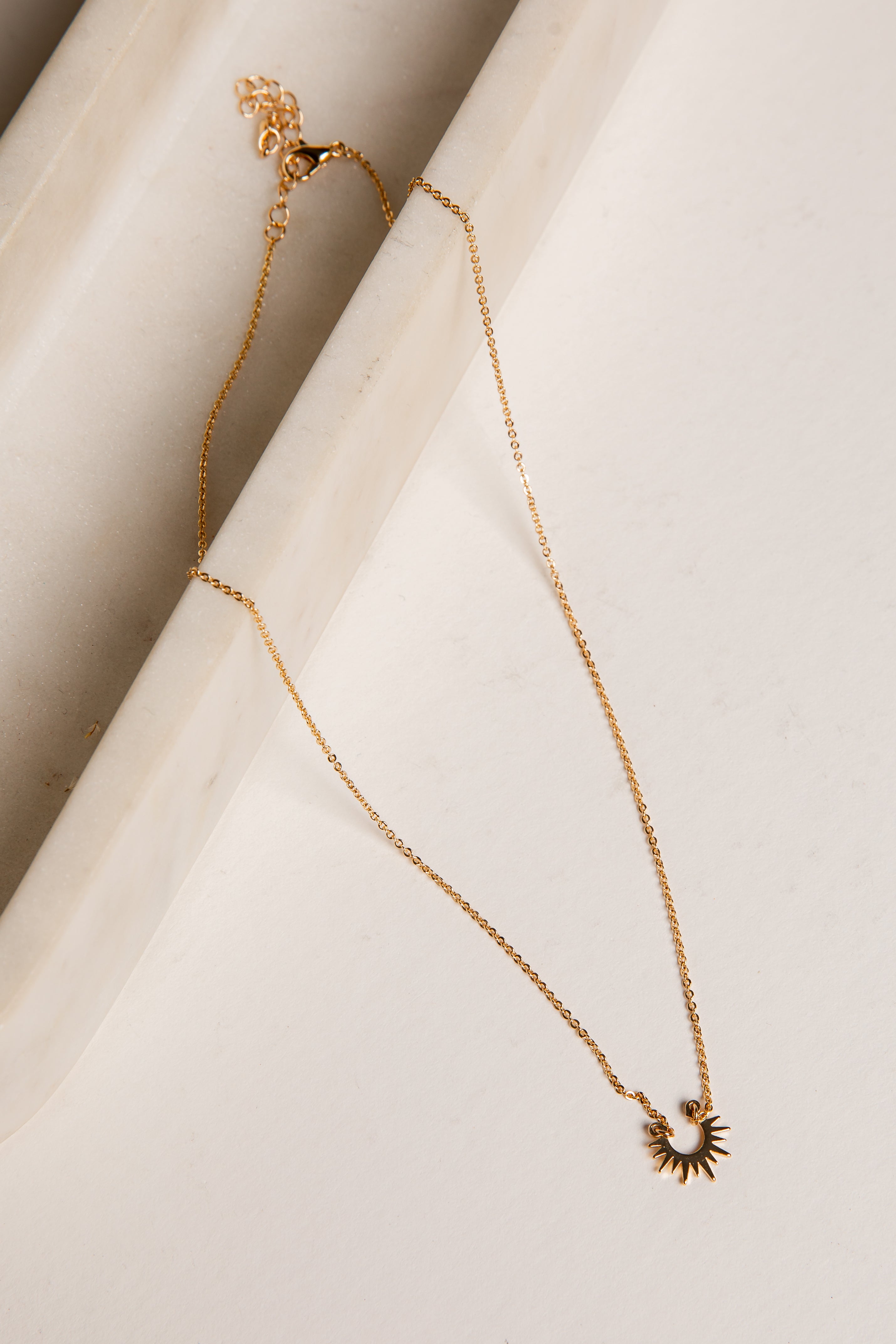 Gold necklace with a sun pendant on a light background