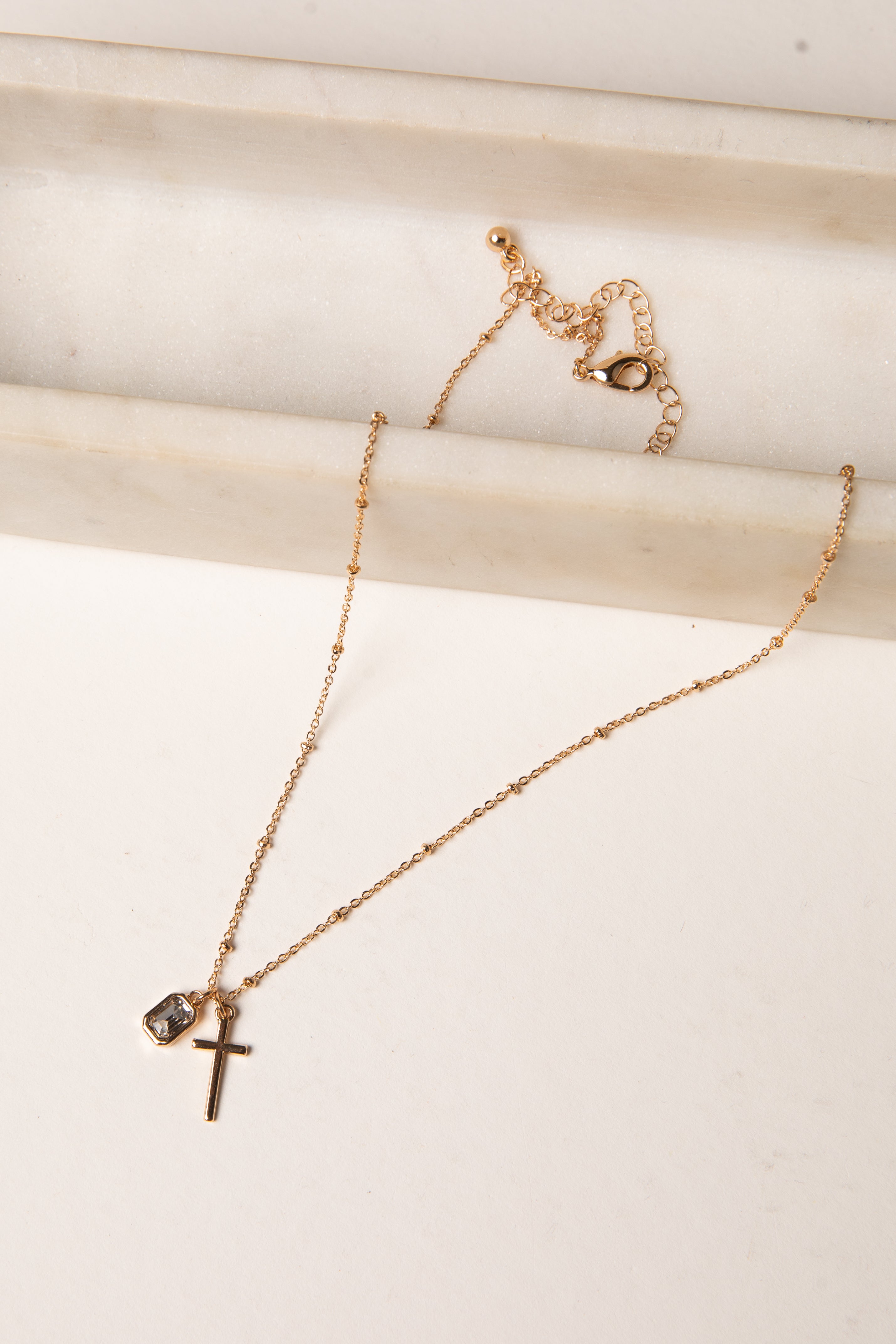 Gold necklace with a cross pendant on a light wooden surface