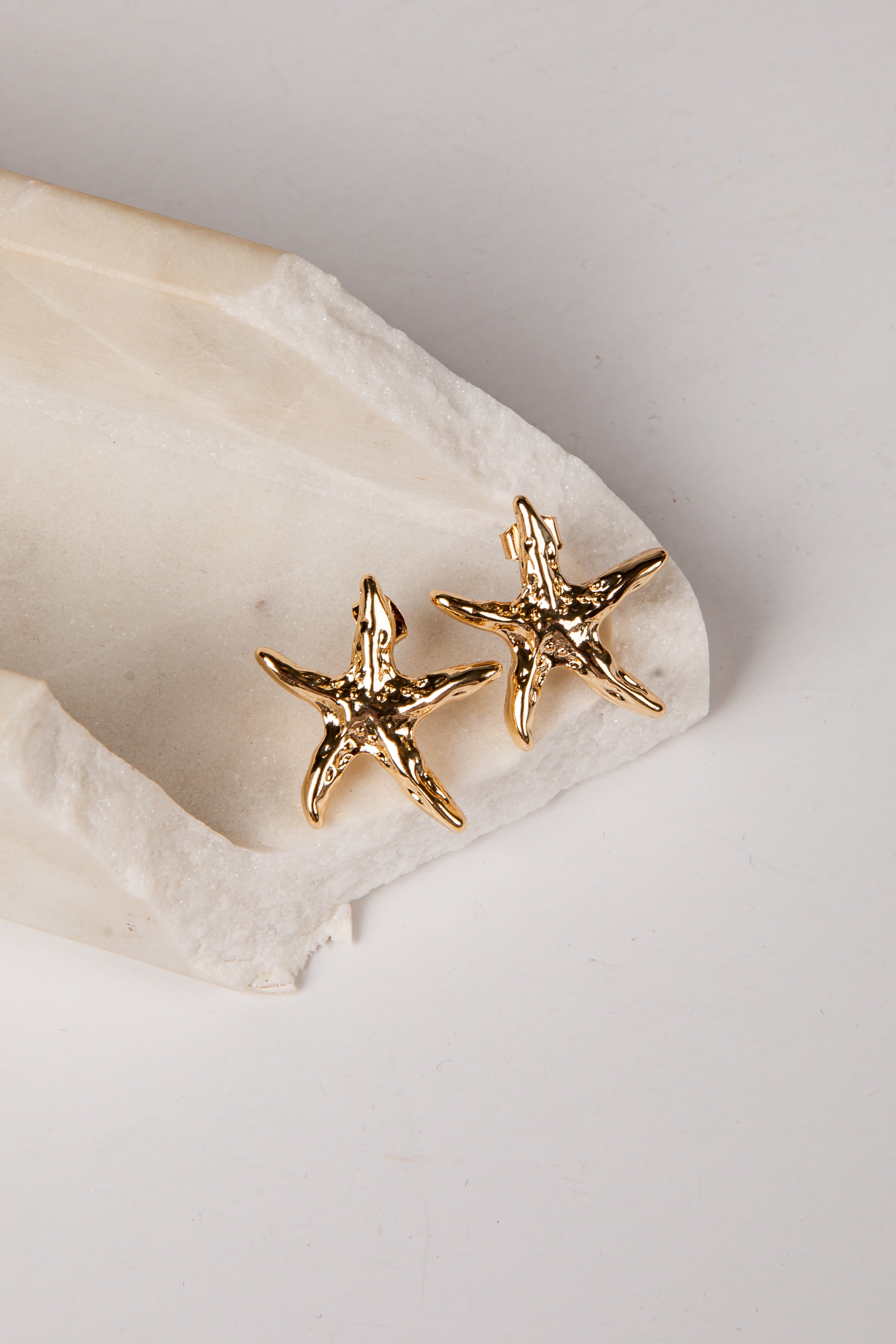 Gold starfish earrings on a white stone surface