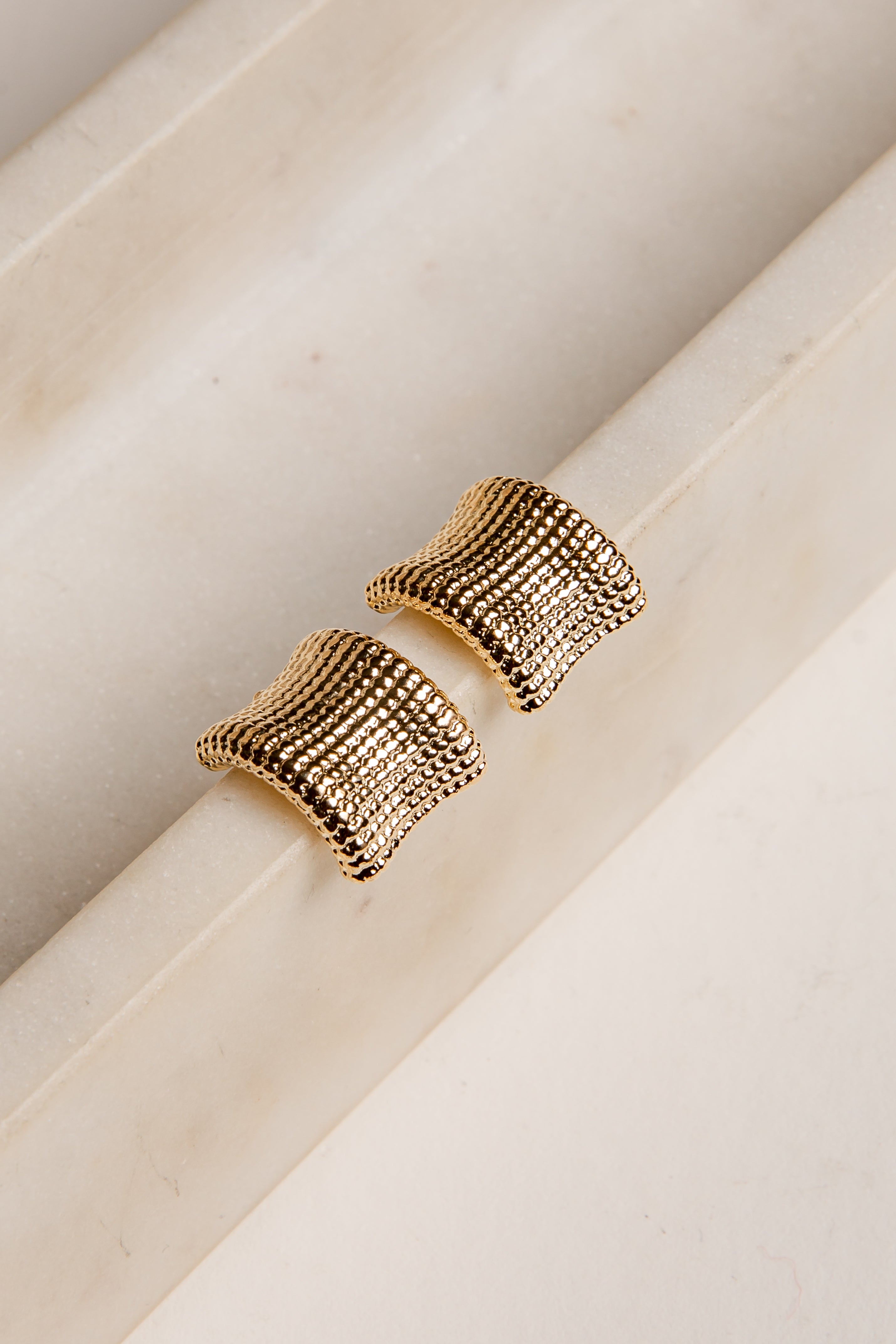 Gold textured earrings on a marble surface