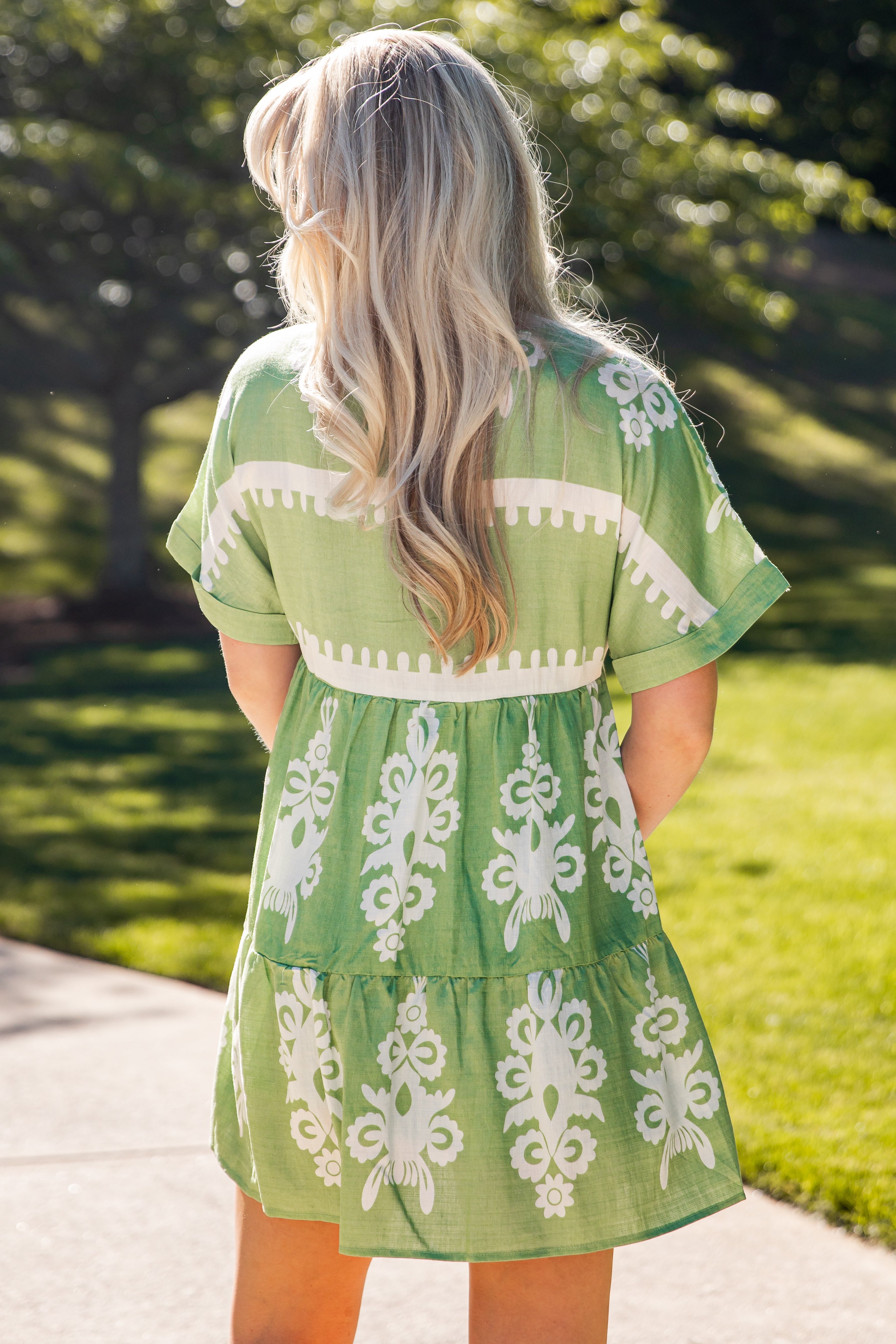 Woman wearing a green dress with white patterns walking on a path.