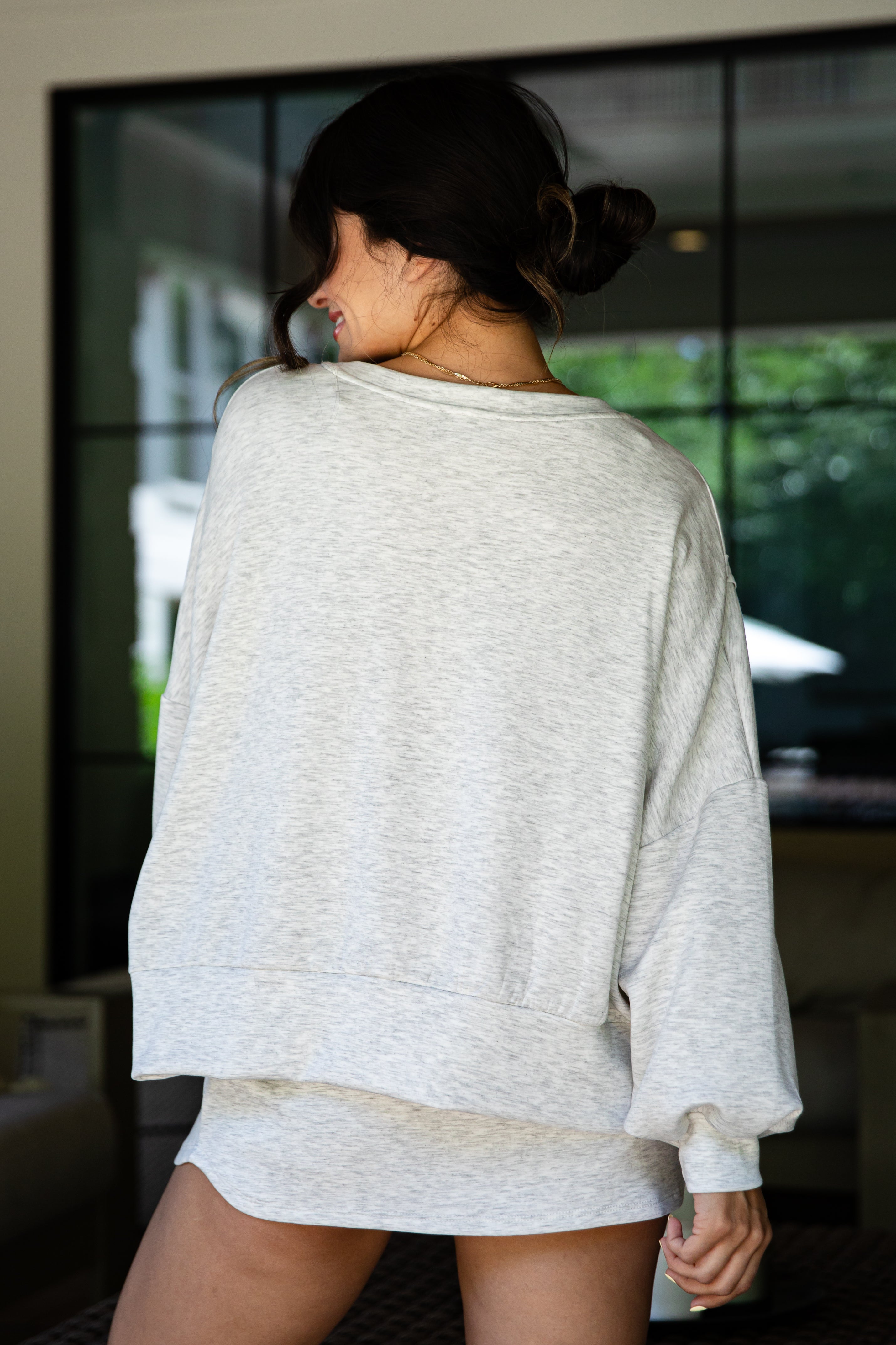 Woman wearing a grey oversized sweatshirt in an indoor setting