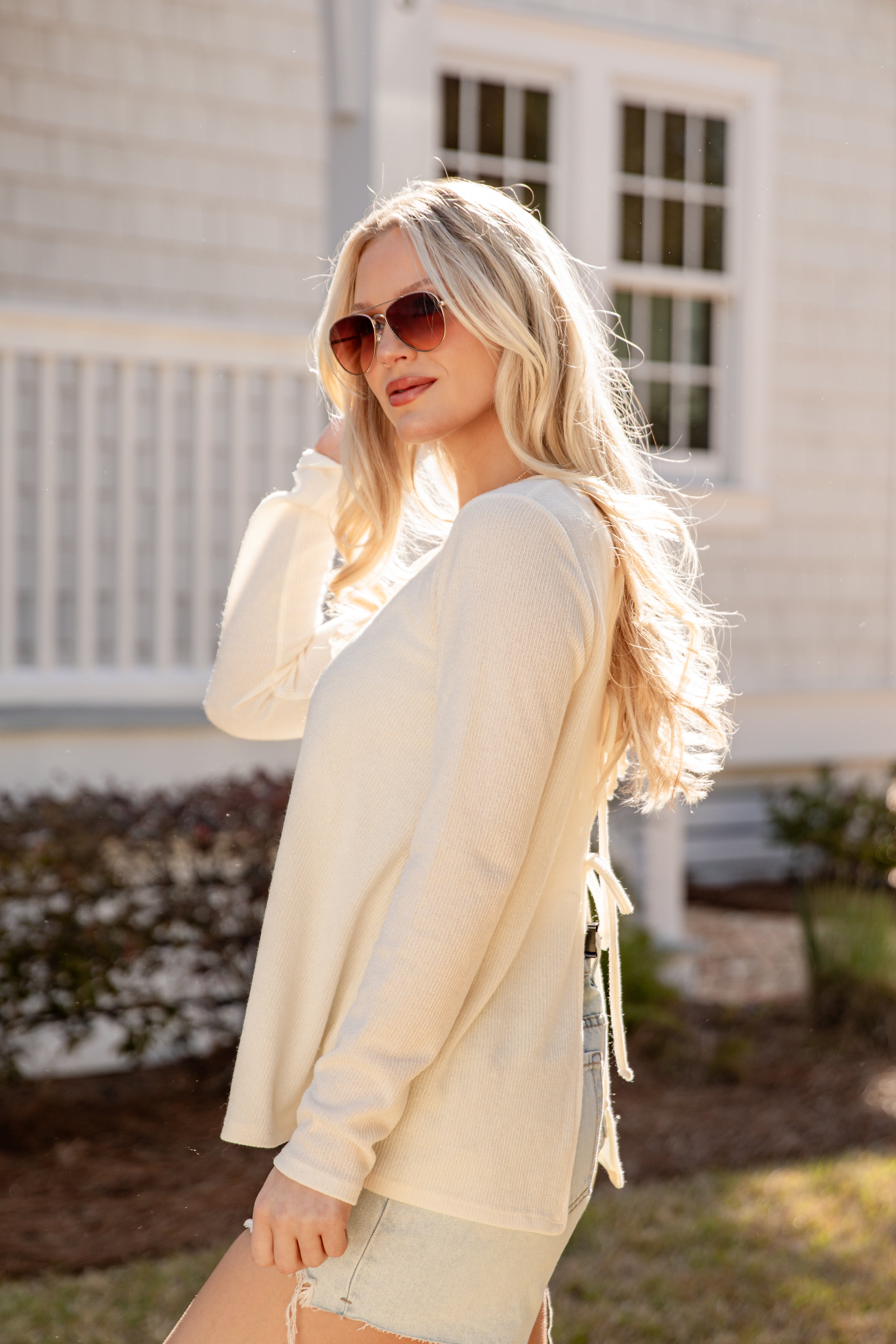 Woman wearing a light-colored cardigan and sunglasses outdoors.