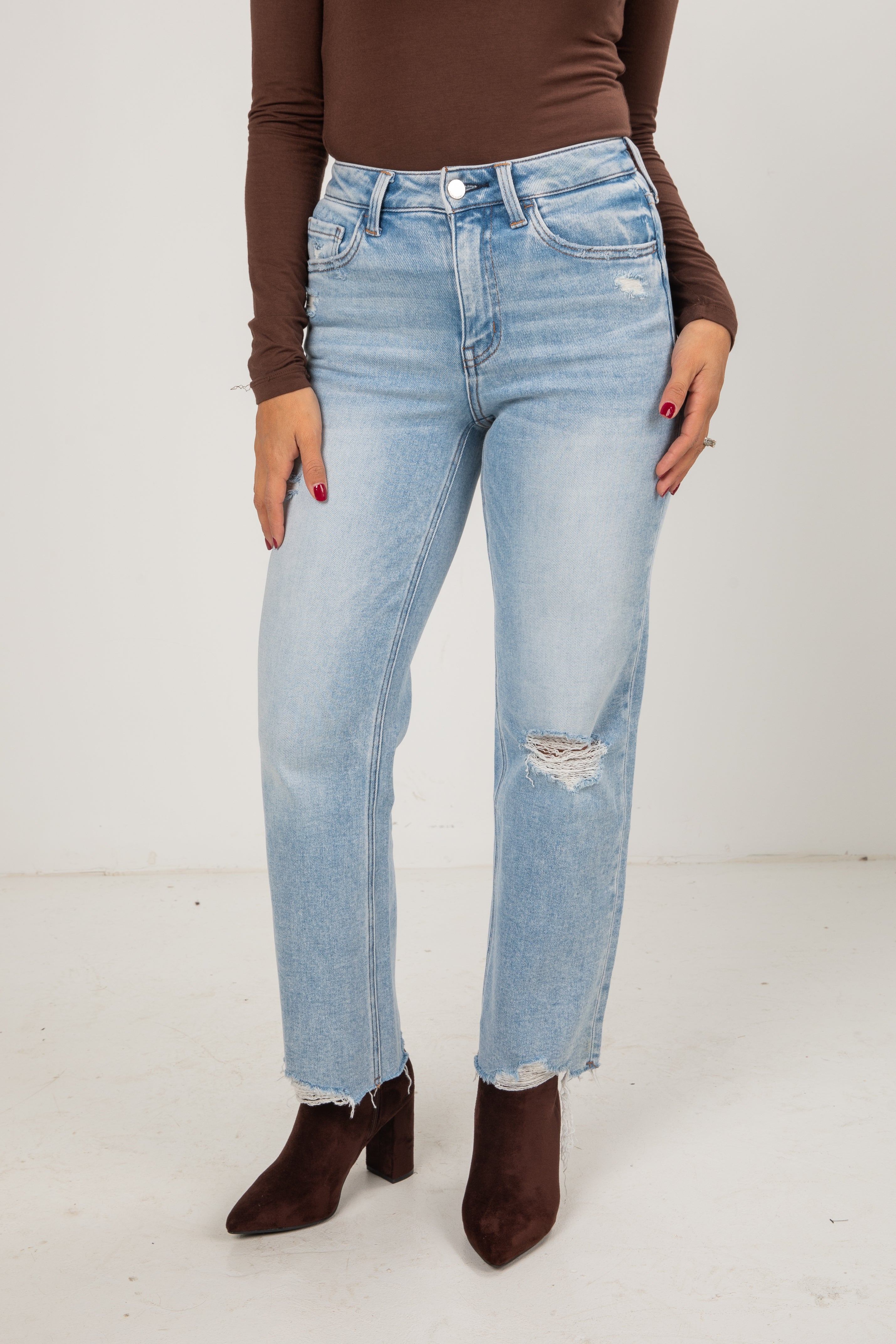 Person wearing light blue jeans and brown shoes on a white background