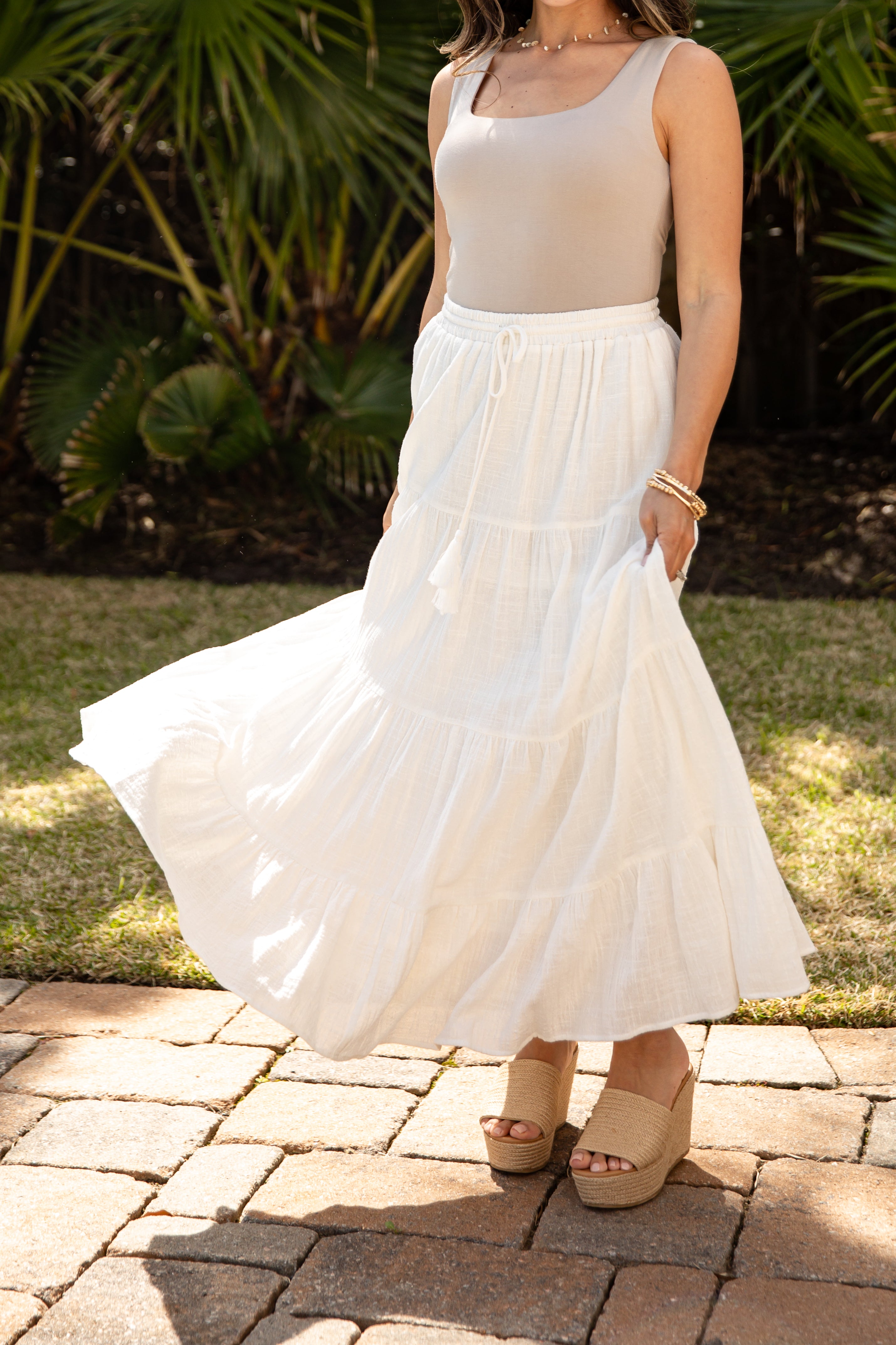 Person wearing a white dress standing on a paved area with greenery in the background