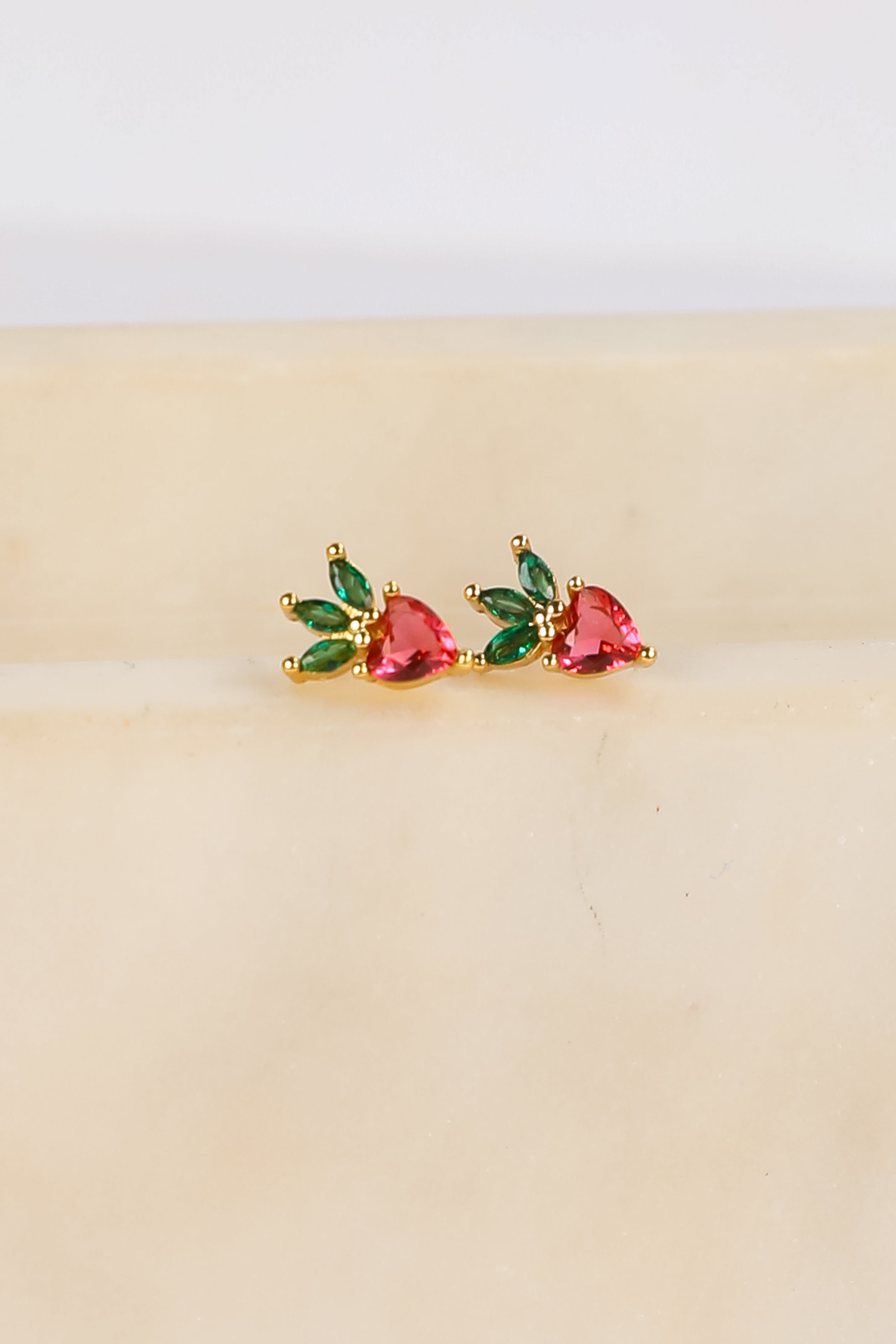 Pair of earrings with red and green gemstones on a beige background