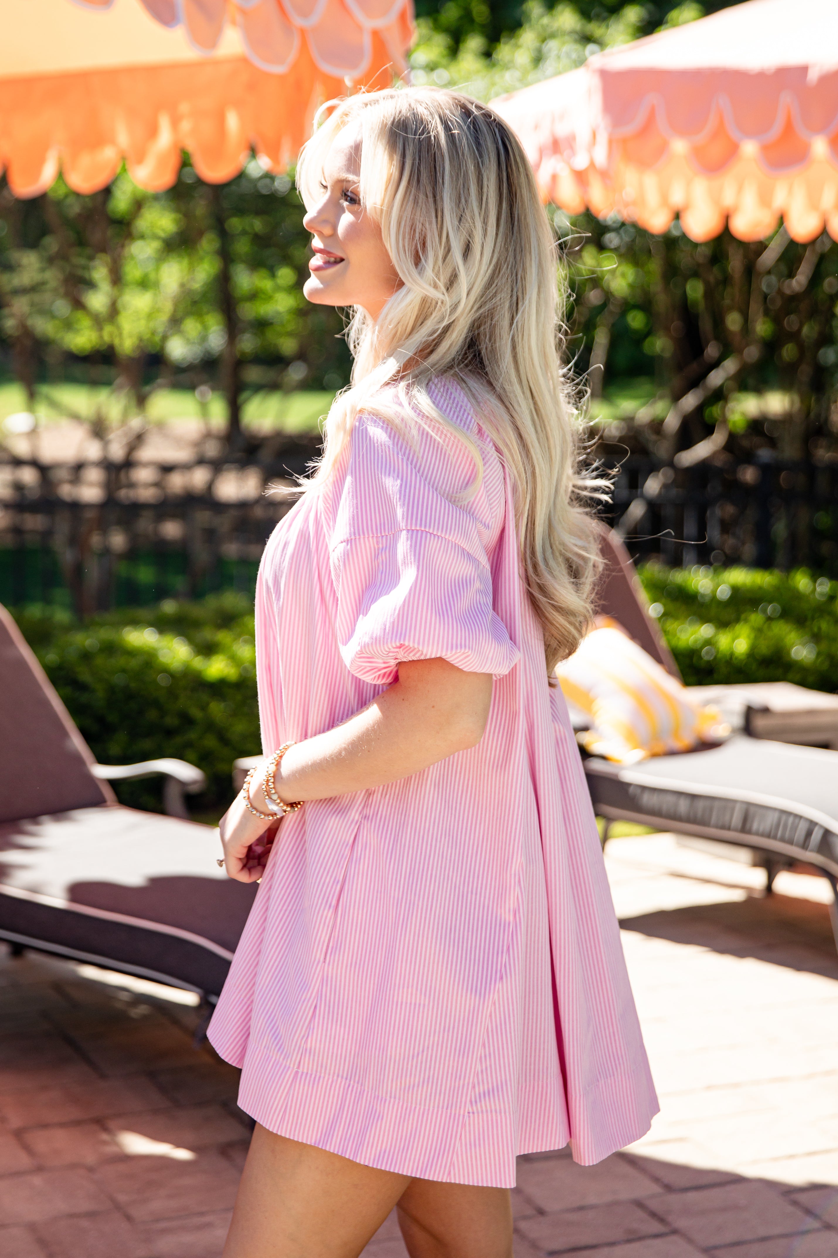 Woman in a pink dress standing outdoors under orange umbrellas.