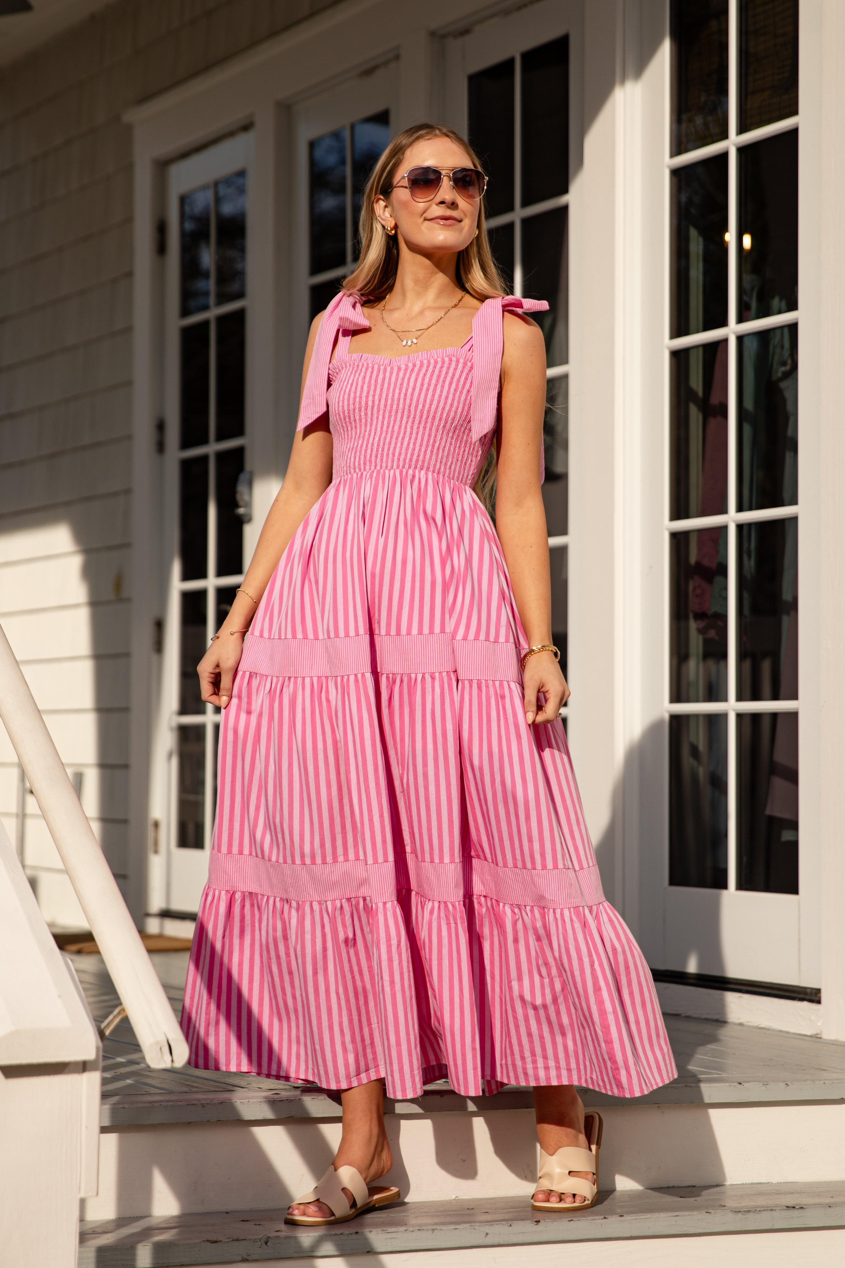 Woman wearing a pink striped dress standing on a porch.