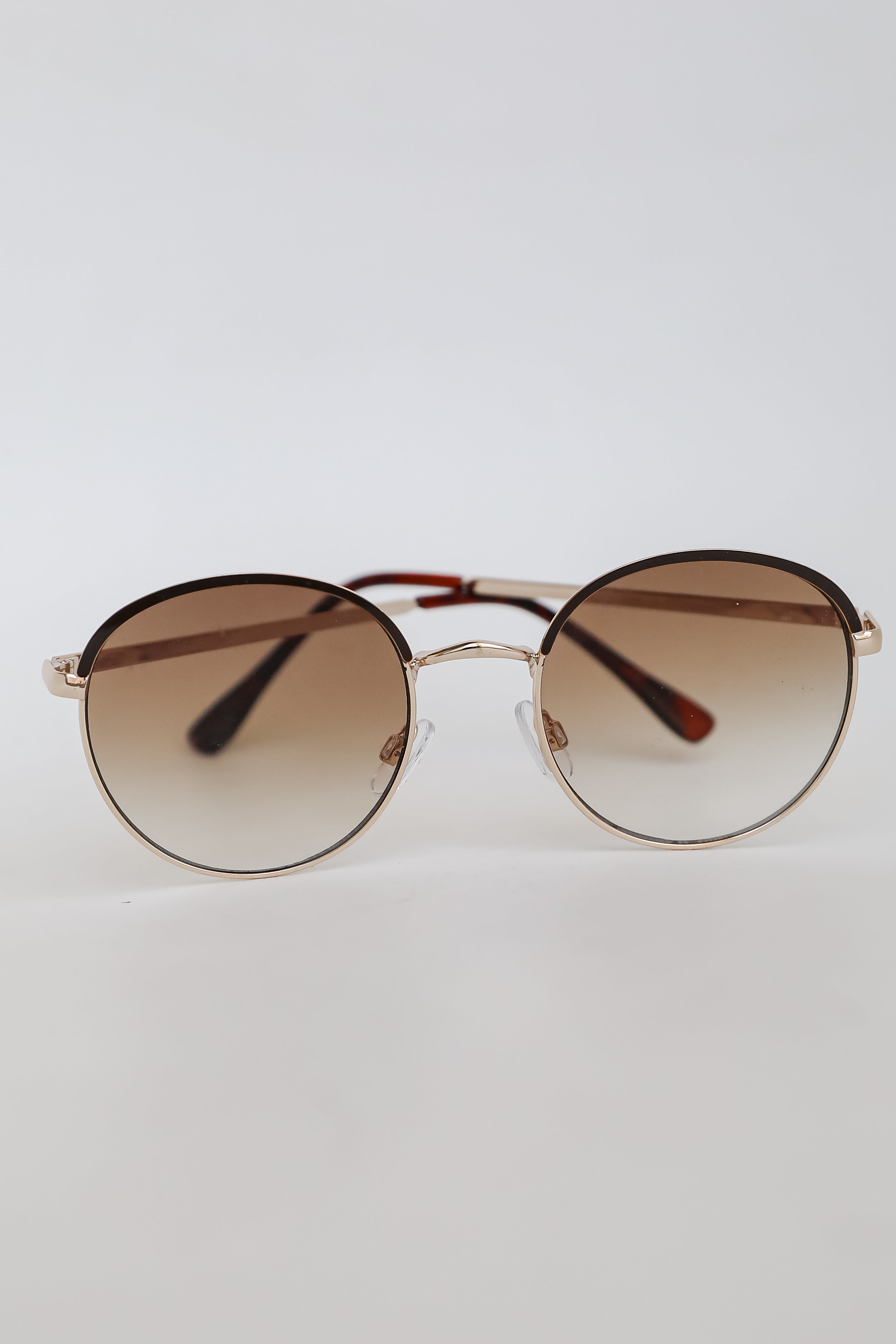 Round sunglasses with gold frame and brown gradient lenses on a light gray background