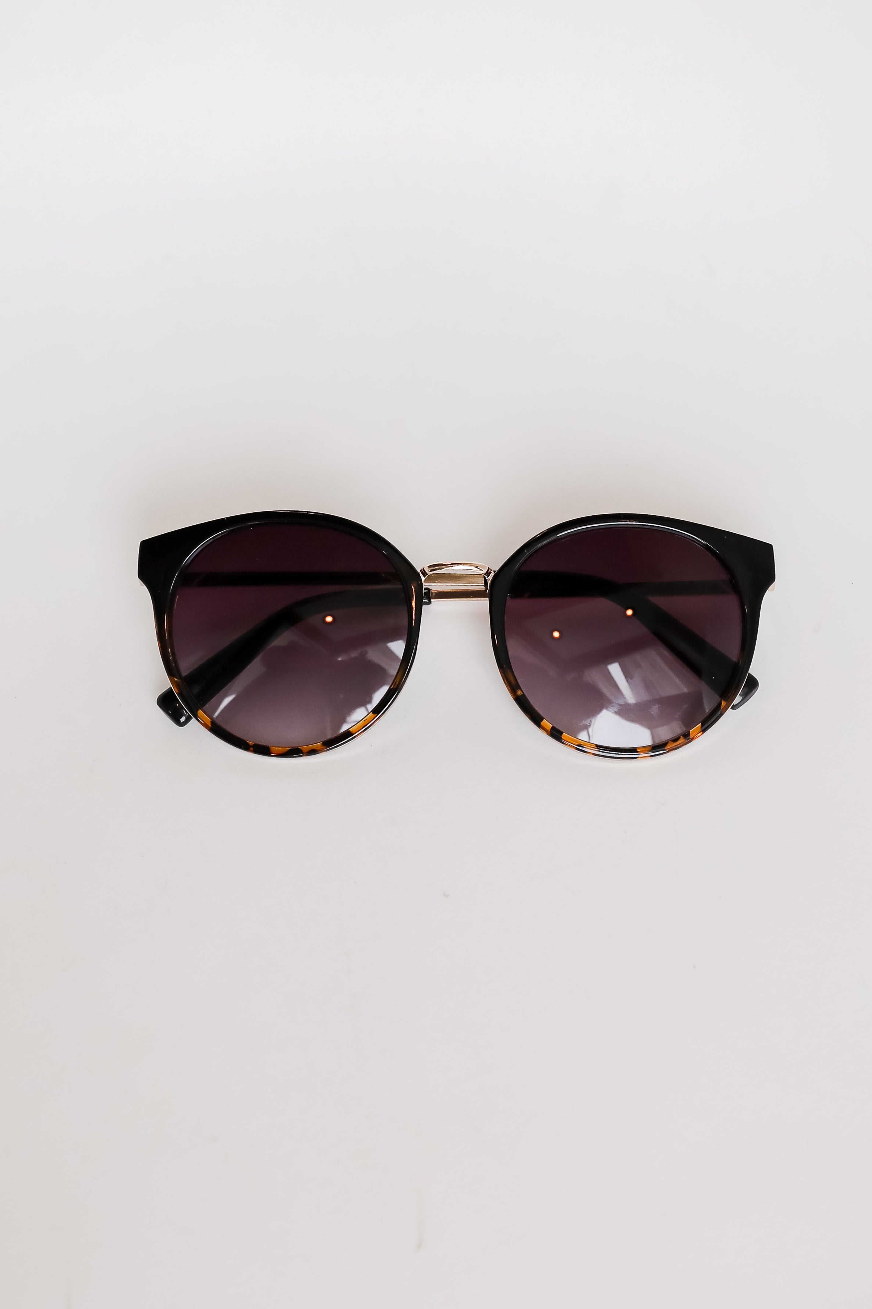 Sunglasses with dark lenses and tortoiseshell frame on a light gray background