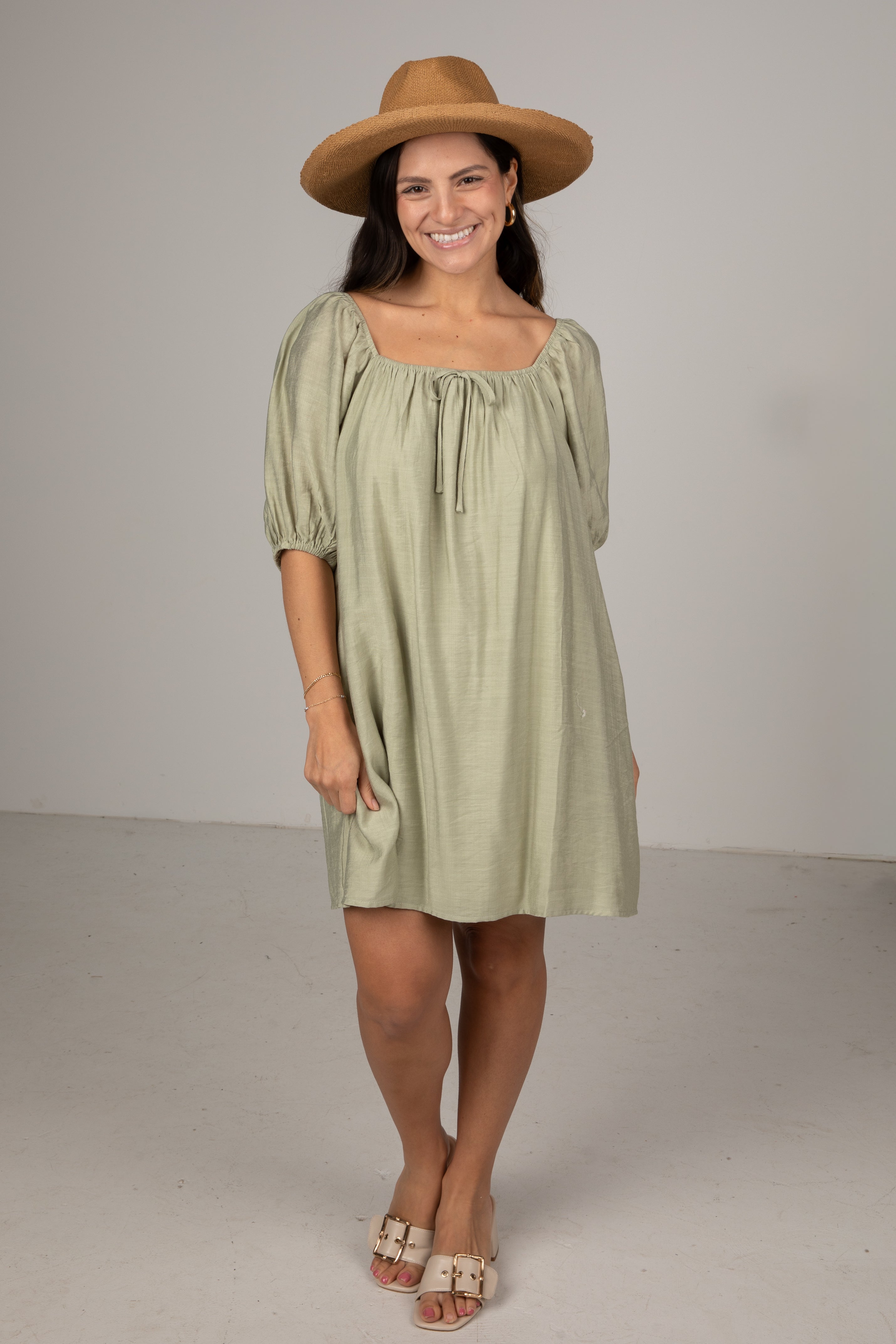 Woman wearing a green dress and brown hat against a plain background