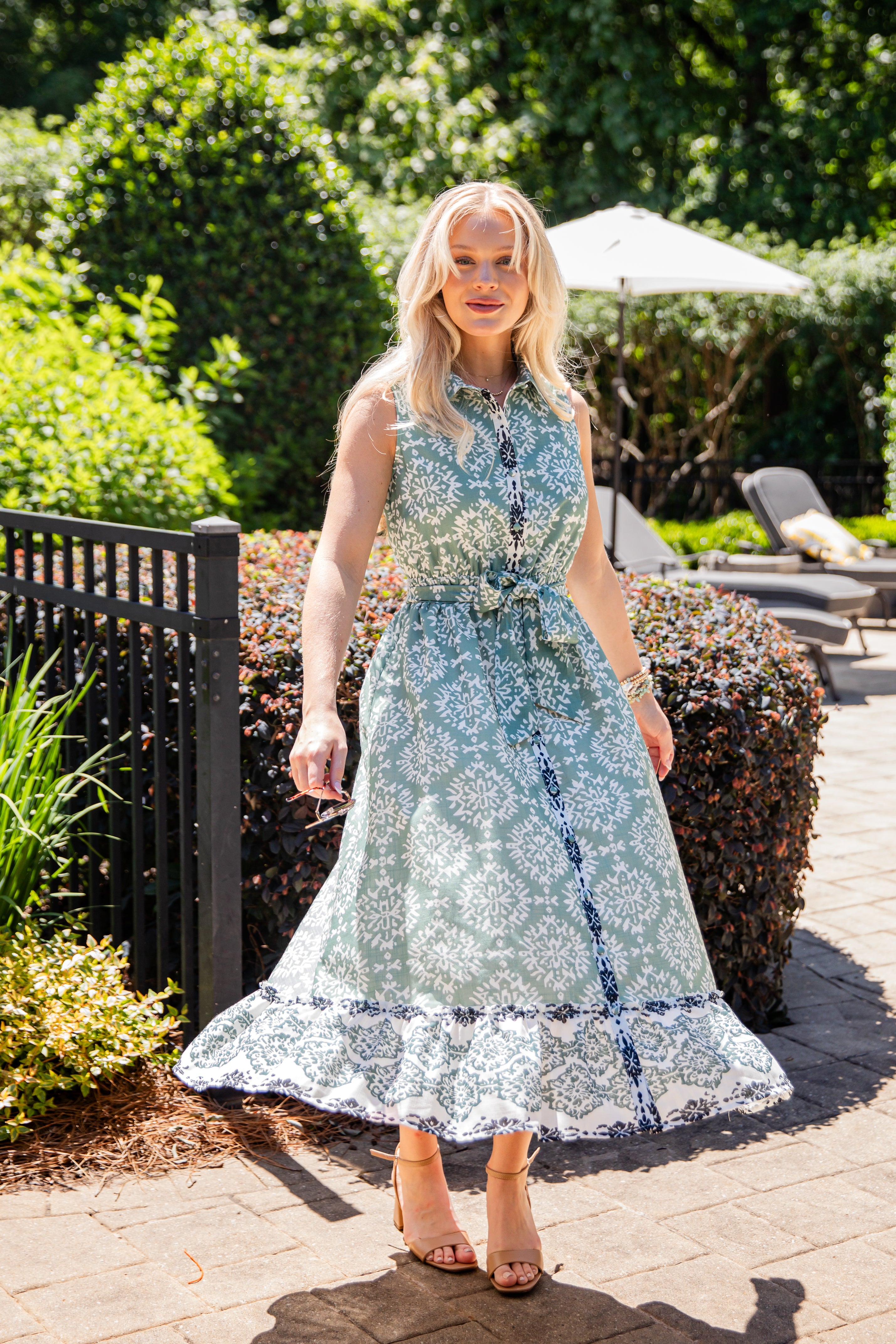 Woman in a floral dress standing outdoors with greenery and a pool area in the background