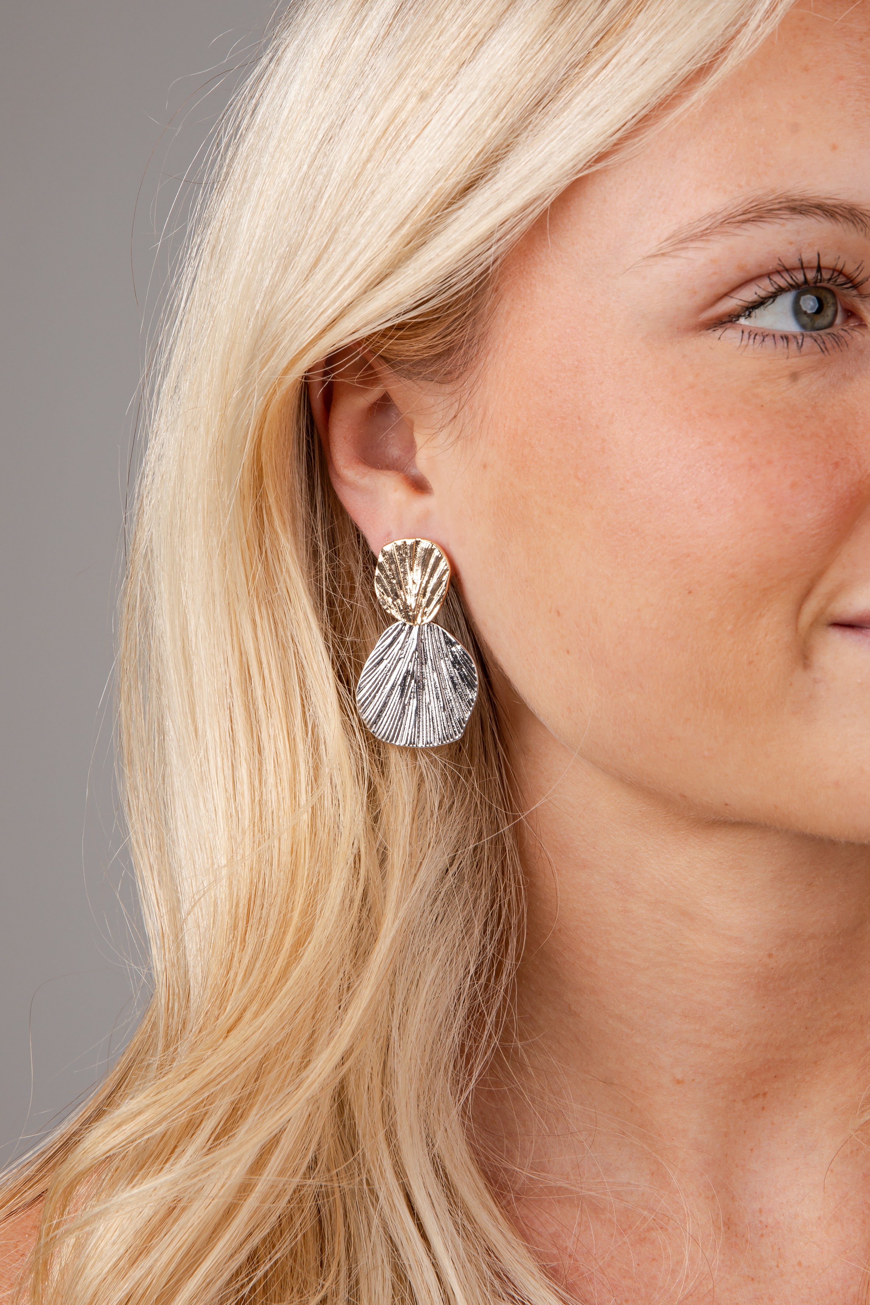 Close-up of a woman wearing a shell-shaped earring with a clear stone.