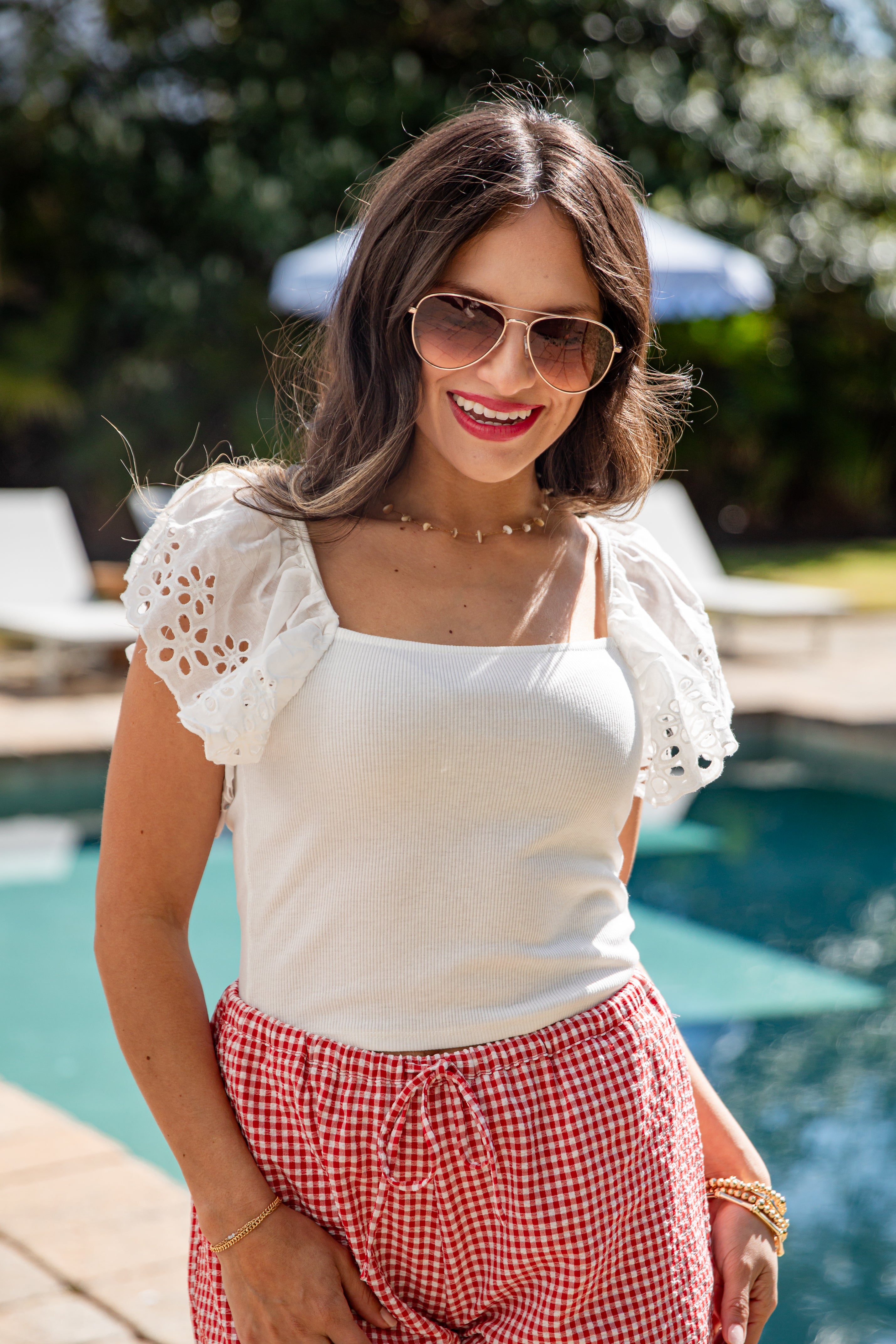 Woman in white top and red patterned shorts smiling poolside.