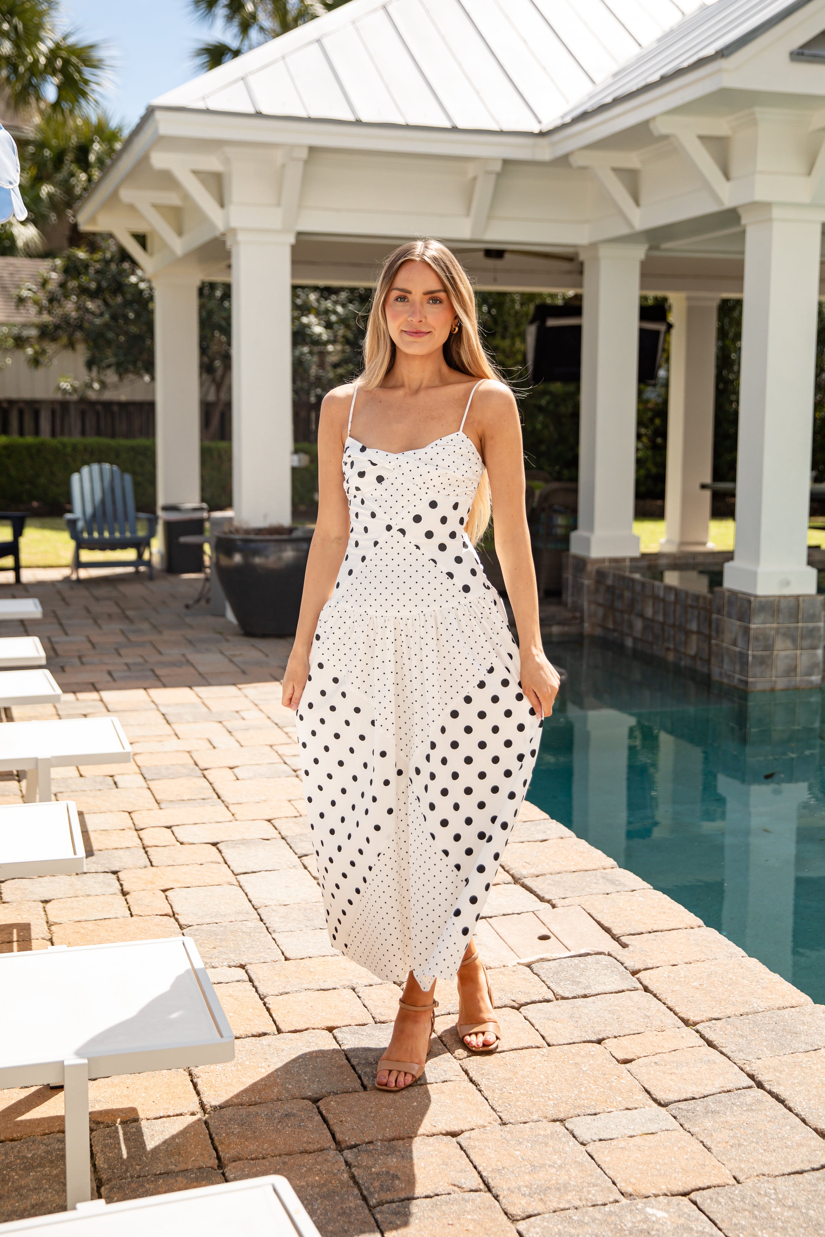 Woman in a polka dot dress standing by a poolside gazebo.
