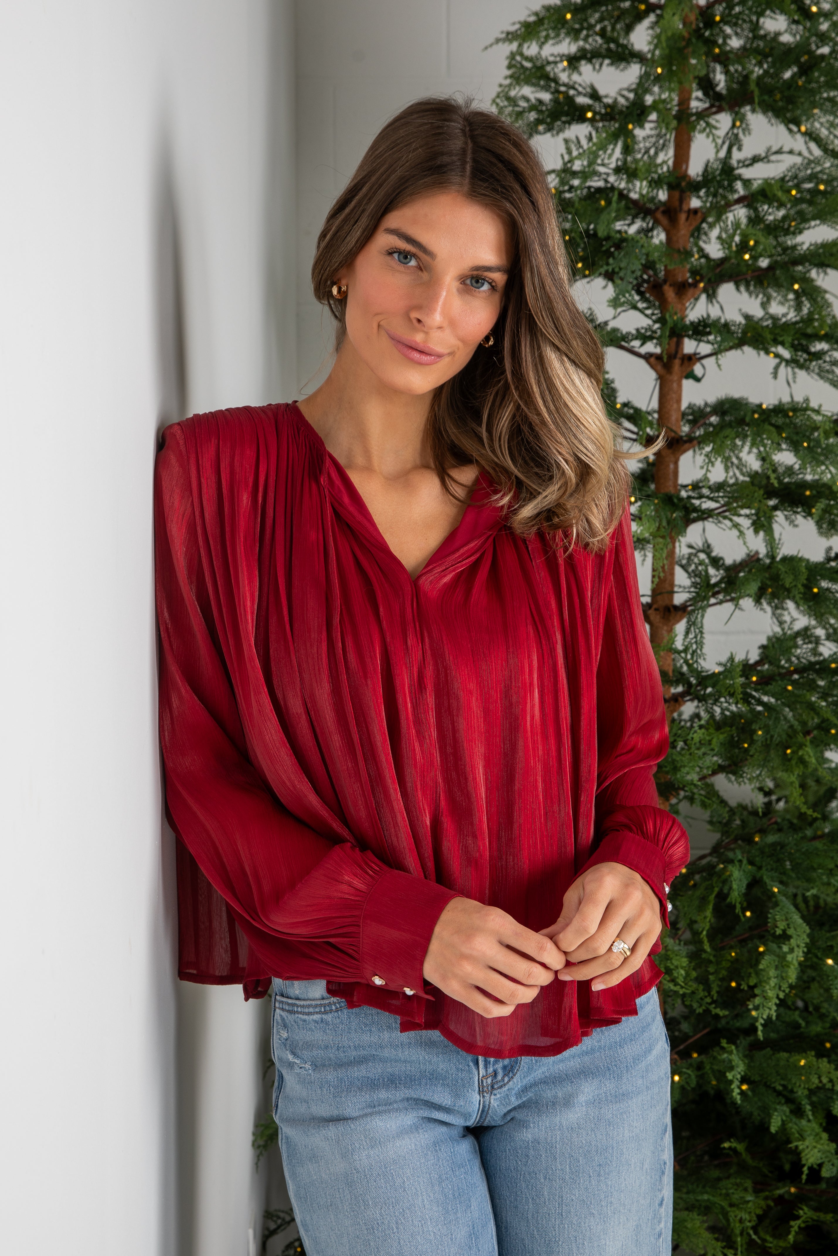 Woman wearing a red blouse and blue jeans standing next to a Christmas tree.