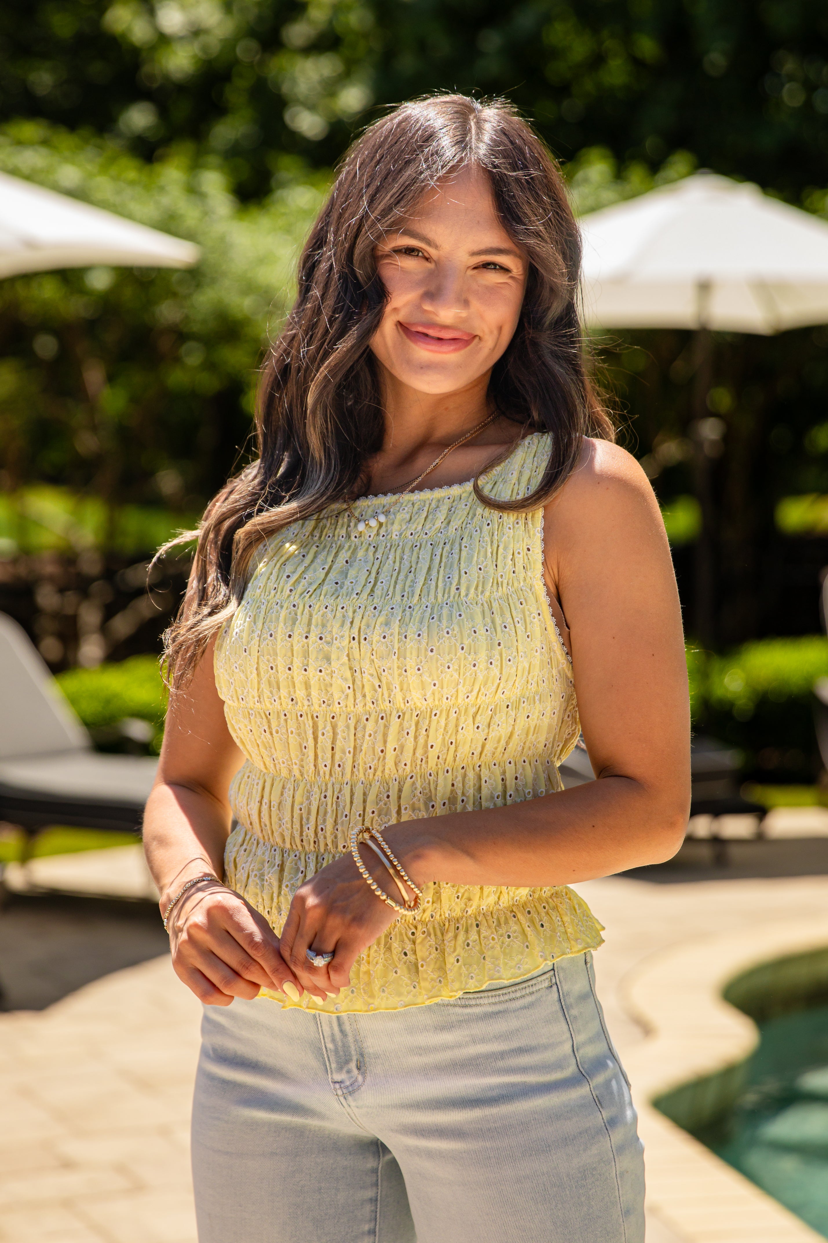 Woman standing outdoors with greenery and a pool in the background