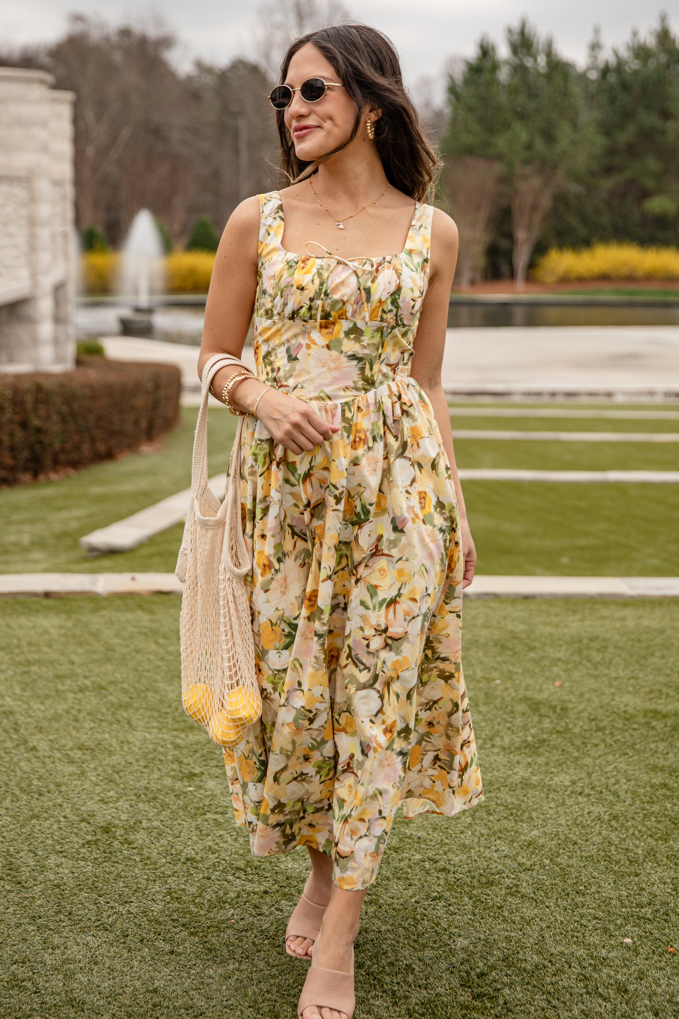 Woman in a floral dress standing on grass with a fountain in the background