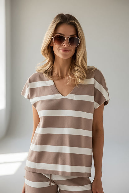 A woman wearing a brown and white horizontally striped short-sleeve V-neck top and matching striped pants, styled with sunglasses, in a brightly lit indoor setting.