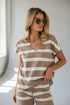 A woman wearing a brown and white horizontally striped short-sleeve V-neck top and matching striped shorts, styled with sunglasses, in a brightly lit room.