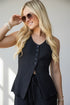 A woman wearing a sleeveless black textured knit vest with a button-front closure and drawstring waist, styled with sunglasses and bracelets against a light gray background.
