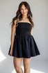 A woman modeling a strapless black mini dress with a flared skirt, standing against a light gray studio background with soft shadows.