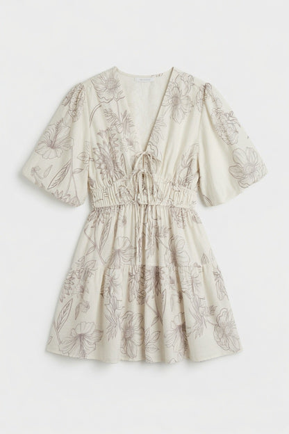 A short-sleeve cream-colored dress with a brown floral line-art print, featuring a V-neckline with a tie-front detail and a gathered smocked waist.