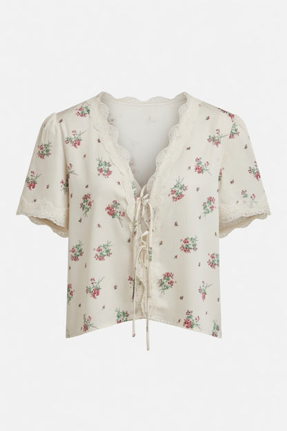 An off-white short-sleeve blouse with a delicate pink and green floral print, featuring a lace-trimmed V-neckline and front tie closure, shown against a plain white background.