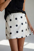 A model wearing a white A-line mini skirt with large black polka dots, paired with a black sleeveless top.