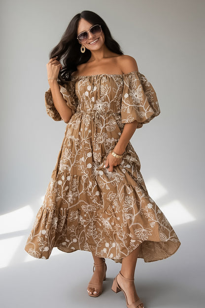 A woman modeling an off-the-shoulder midi dress with a brown and beige floral pattern, paired with sunglasses and beige heels, set against a neutral gray studio background.