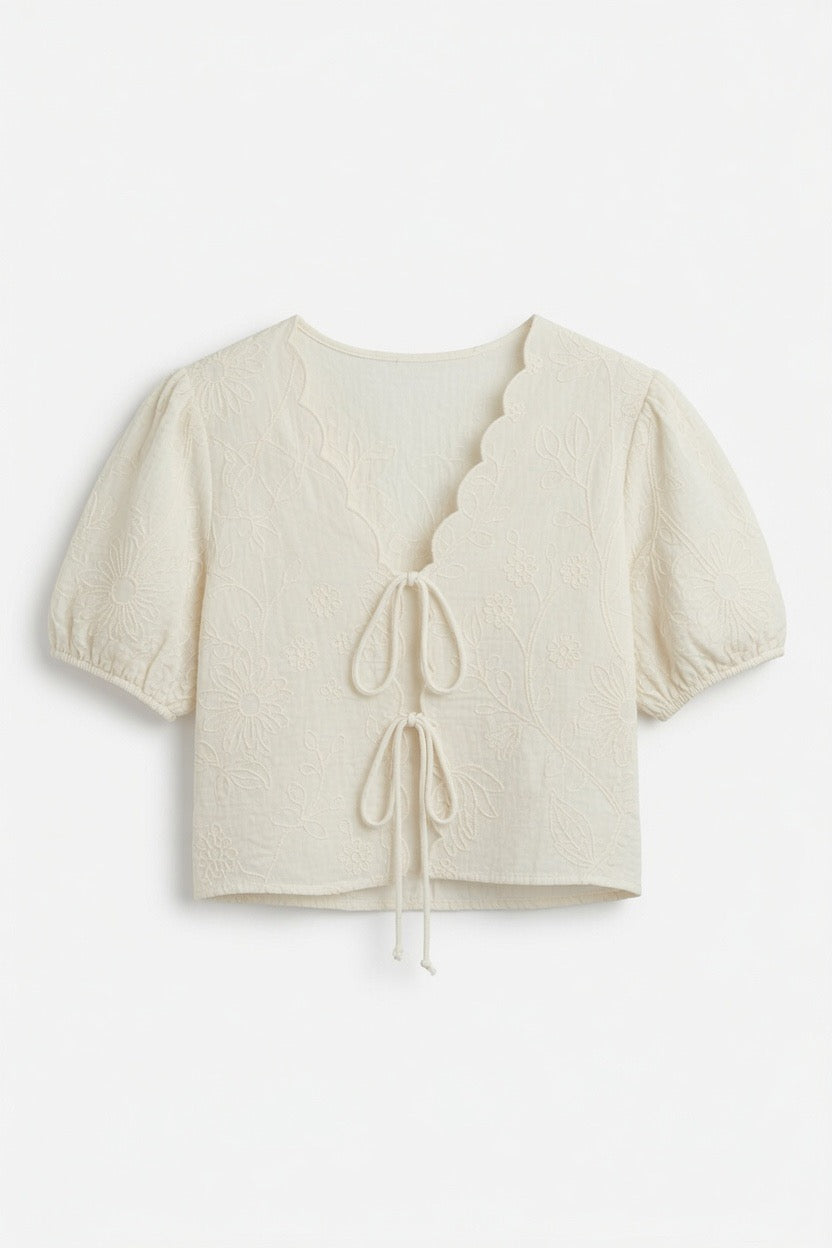 An off-white cropped short-sleeve top with a scalloped V-neckline, tie-front detail, and puff sleeves, shown against a plain white background.
