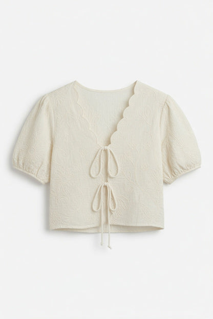 An off-white cropped short-sleeve top with a scalloped V-neckline, tie-front detail, and puff sleeves, shown against a plain white background.