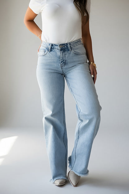 A model wearing light-wash, high-rise, wide-leg jeans paired with a white t-shirt and pointed-toe flats, shown from the chest down against a neutral studio background.