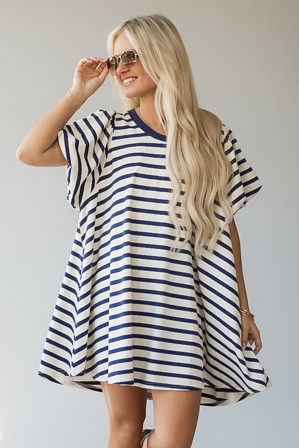 A woman modeling a loose, short-sleeve tunic-style dress with navy blue and white horizontal stripes, photographed against a plain light gray studio background.