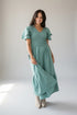 A woman wearing a sage green tiered maxi dress with ruffled short sleeves and smocked detailing