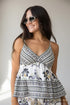 A woman wearing a sleeveless white camisole top with black and navy blue bohemian-style patterns, paired with matching patterned bottoms and round sunglasses, set against a plain light gray background.