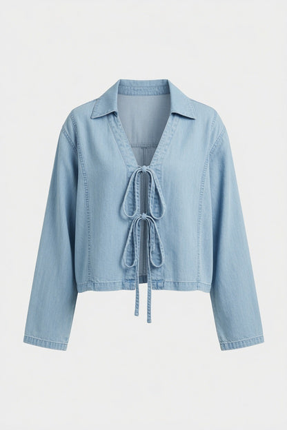 A light blue denim cropped jacket with a tie-front detail, long sleeves, and a pointed collar, shown against a plain light gray background.