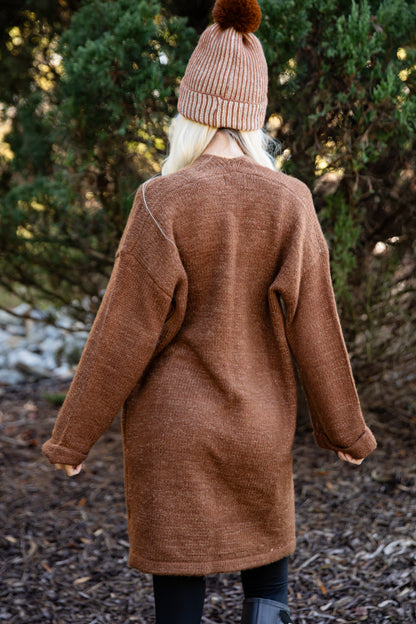 Person wearing a brown coat and pink beanie standing in a forest setting
