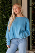 Woman wearing a blue sweater and jeans standing in front of a decorated Christmas tree.