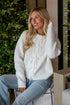 Woman wearing a white sweater with lace details sitting in a festive setting with Christmas decorations.