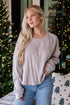 Woman wearing a beige sweater and blue jeans in front of a decorated Christmas tree.
