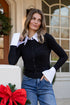 Woman in black cardigan and blue jeans standing in front of a decorated door with a red bow.