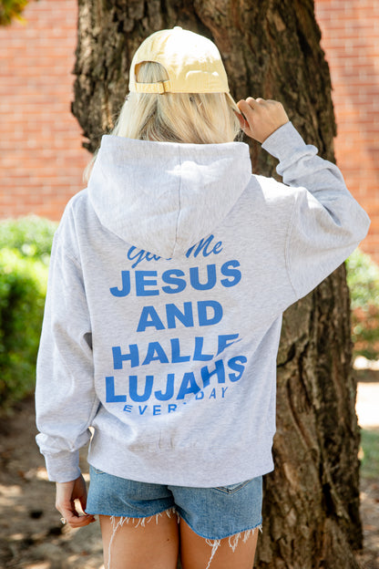 A woman viewed from behind wearing a light gray heather hoodie with bold blue text on the back reading &