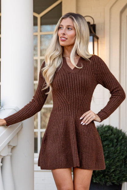 Woman in a brown dress standing on a porch with decorative elements.